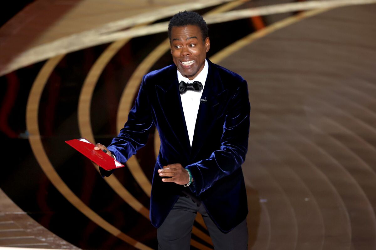 A man in a tuxedo stands at a microphone during the Oscars ceremony.