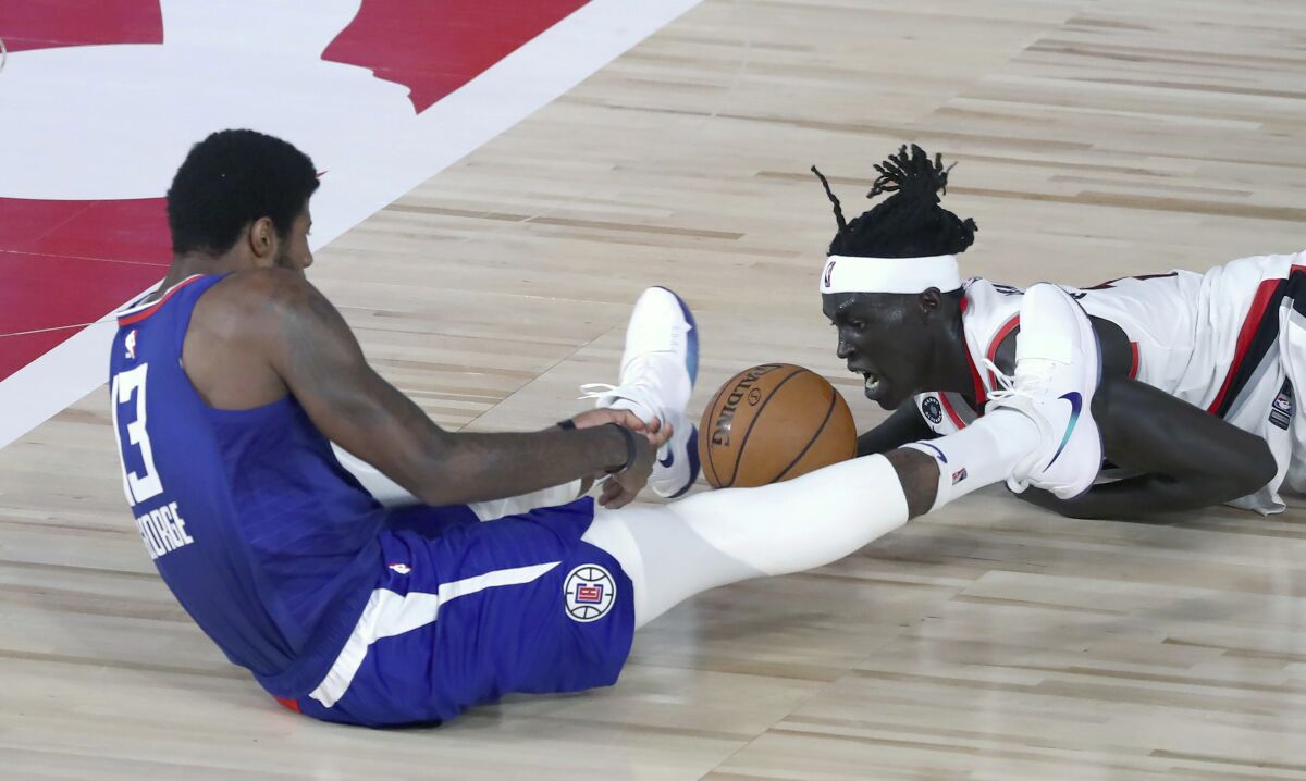 Los Angeles Clippers guard Paul George (13), left, and Portland Trail Blazers forward Wenyen Gabriel (35) battle for a loose ball during the first half of an NBA basketball game Saturday, Aug. 8, 2020, in Lake Buena Vista, Fla. (Kim Klement/Pool Photo via AP)