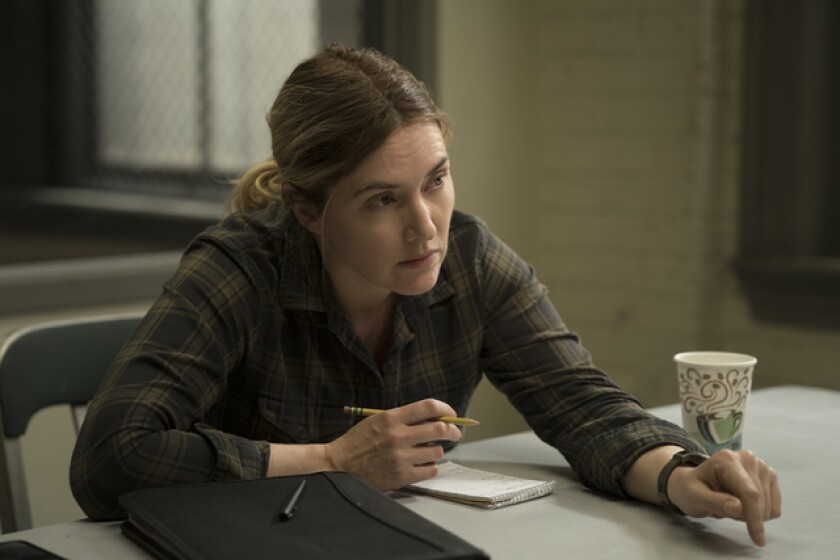 A woman in a flannel shirt sits at a table with a pencil, notebook and cup of coffee