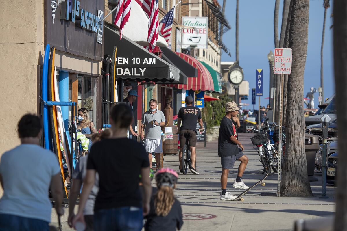 People walk and skateboard on the sidewalk past businesses on West Oceanfront in Newport Beach.