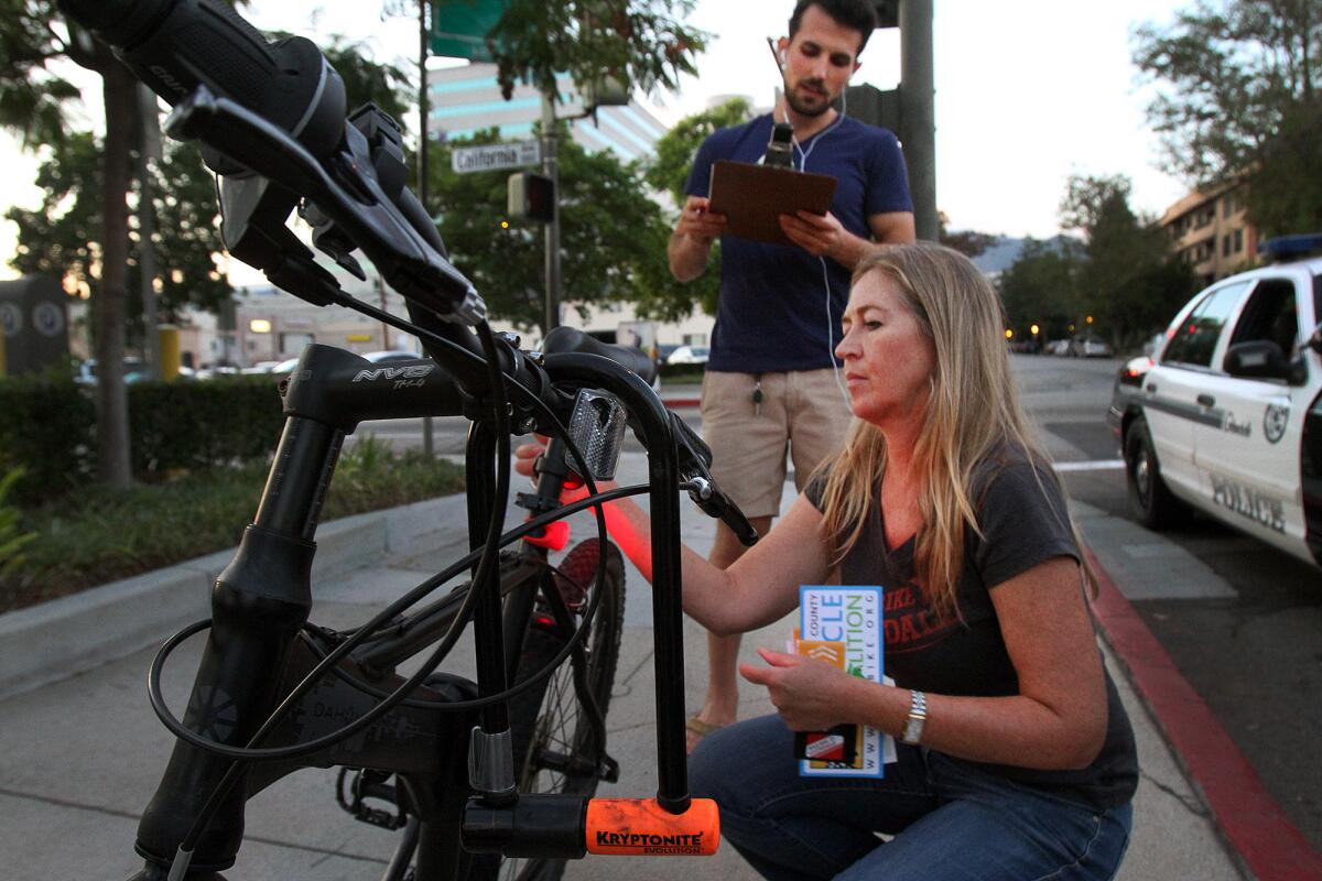 As Chris Chorebanian of Glendale, fills out a questionaire, Nathalie Winiarski of Walk Bike Glendale puts a free rear light on his bicycle as part of Operation Firefly in conjunction with the Los Angeles County Bicycle Coalition and the assistance of the Glendale Police Department on Wednesday, August 20, 2014. Glendale police officers stopped bicyclists riding without lights, but instead of giving them citations, let Winiarski talk with them about safe cycling at night and attached free front and rear lights.