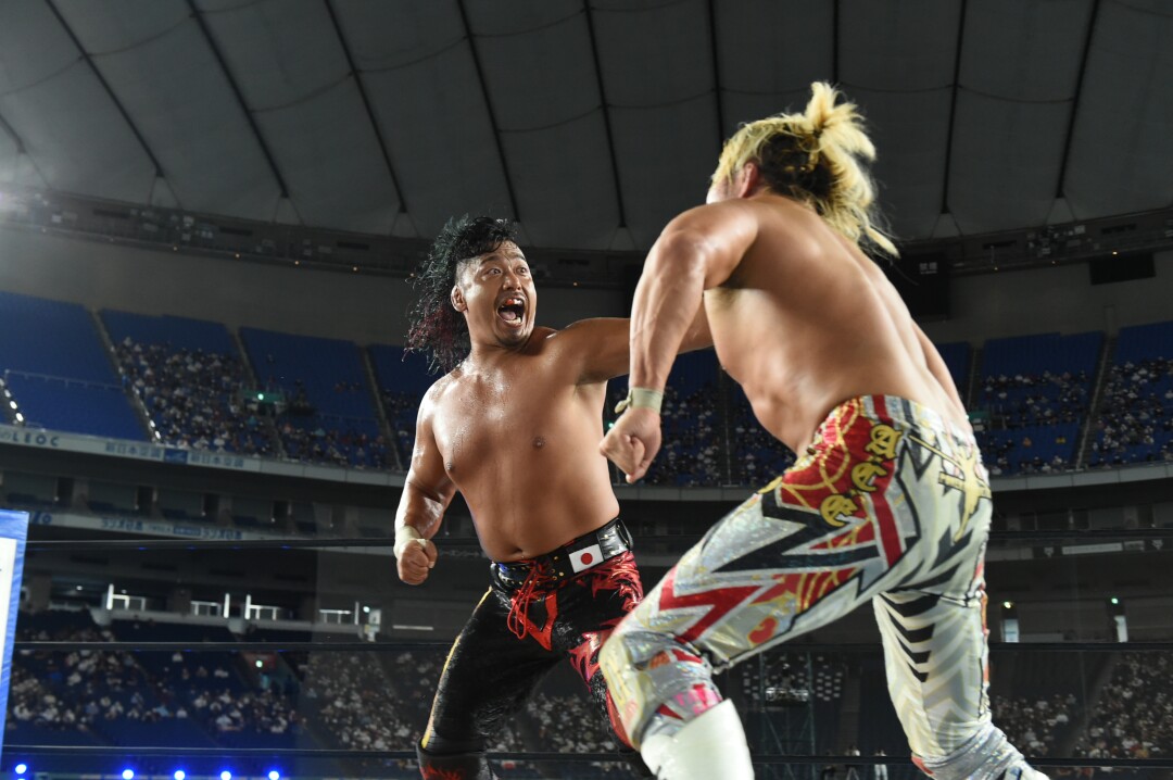 Two bare-chested male pro wrestlers in colorful pants face off in the ring.