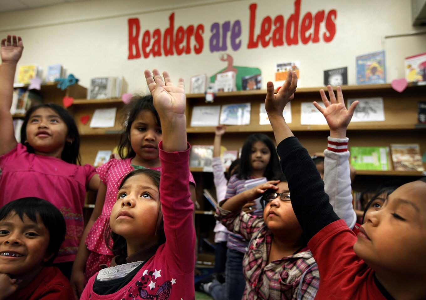 Raising their hands, Alexa Martinez, 7, back row, left; Jennifer Hernandez, 6; Helen Hernandez, 7; and Noe Ortiz, 6, are eager to answer a question from library aide Cindy Ramirez after reading the book "Abe Lincoln's Hat" at San Pedro Elementary School in Los Angeles.