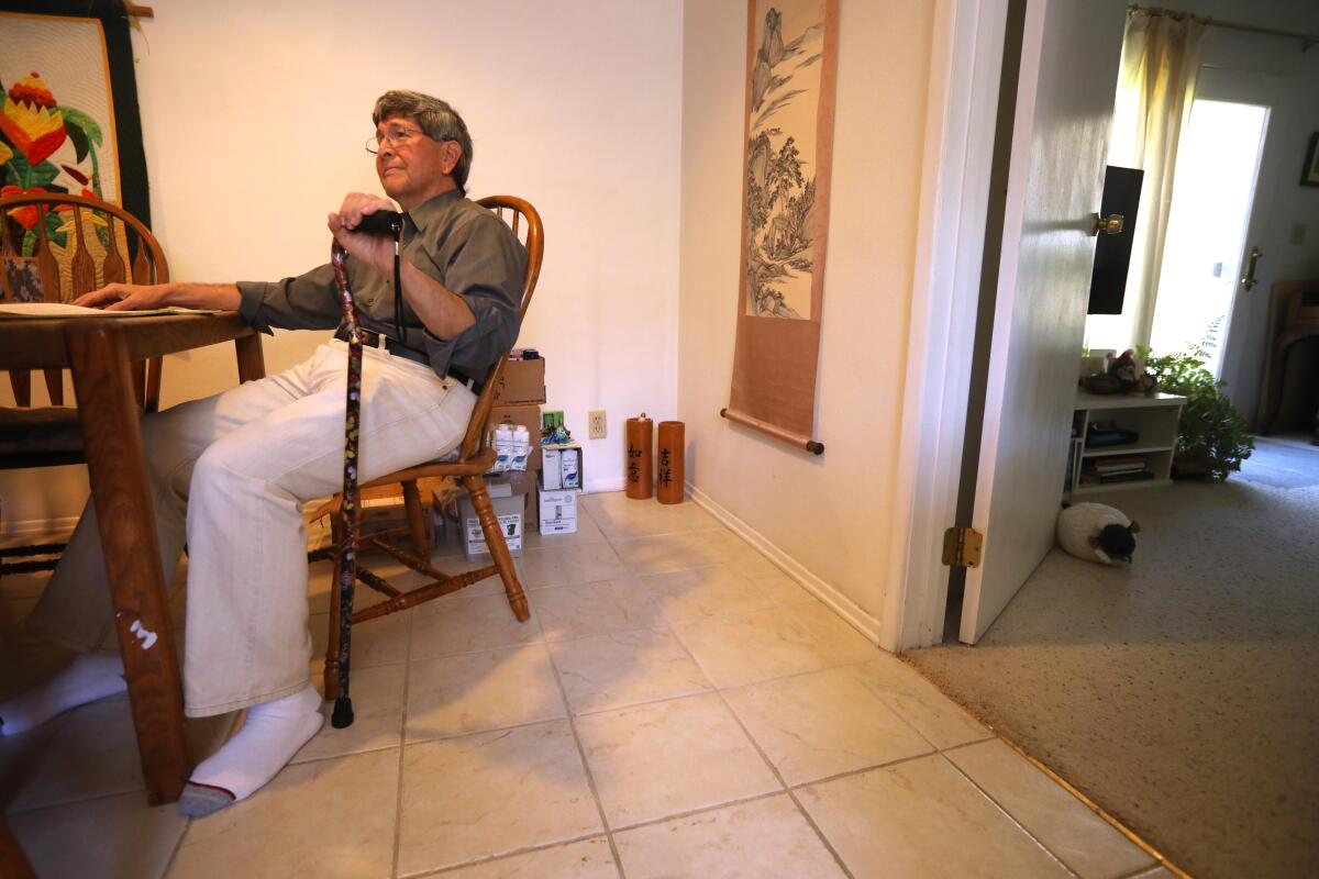 A man using a cane sits at a desk in his home.
