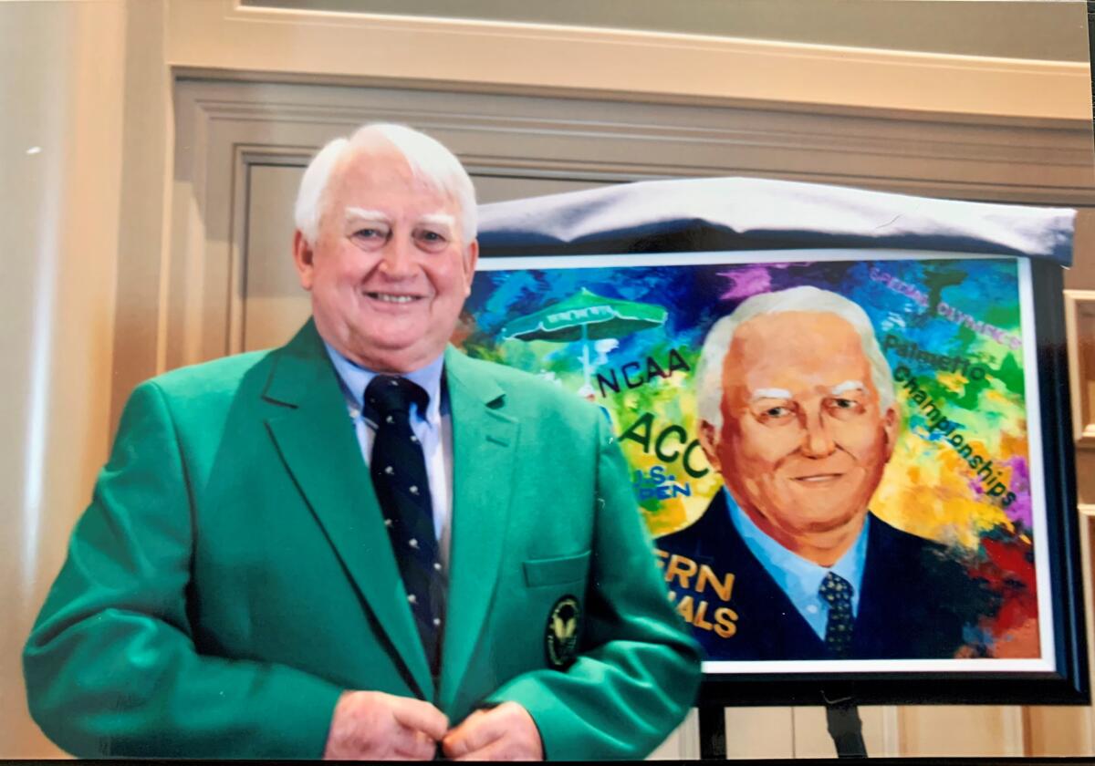 Carey Alexander Washington in a green jacket stands in front of an illustration of himself.