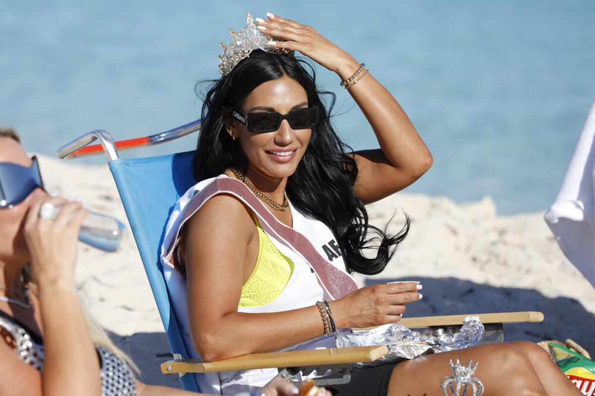 A woman with dark hair sitting in a beach chair wearing a sash and a crown and sunglasses