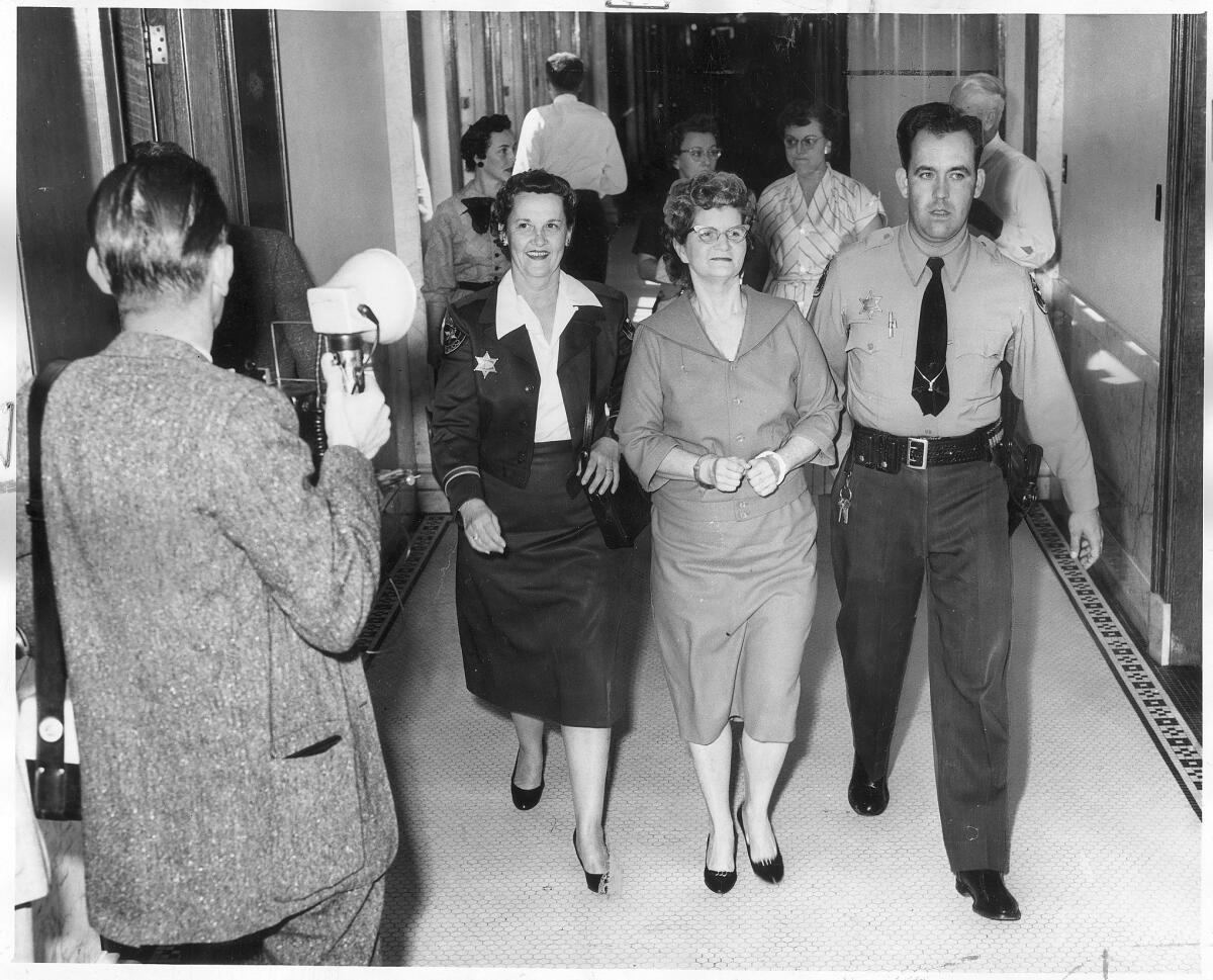 Una foto de archivo del 17 de marzo de 1959, de Elizabeth Ann Duncan, acompañada por el agente Jeff Boyd, con una débil sonrisa en su rostro mientras regresa a su celda para esperar el veredicto del jurado (fotógrafo desconocido / Los Angeles Times).