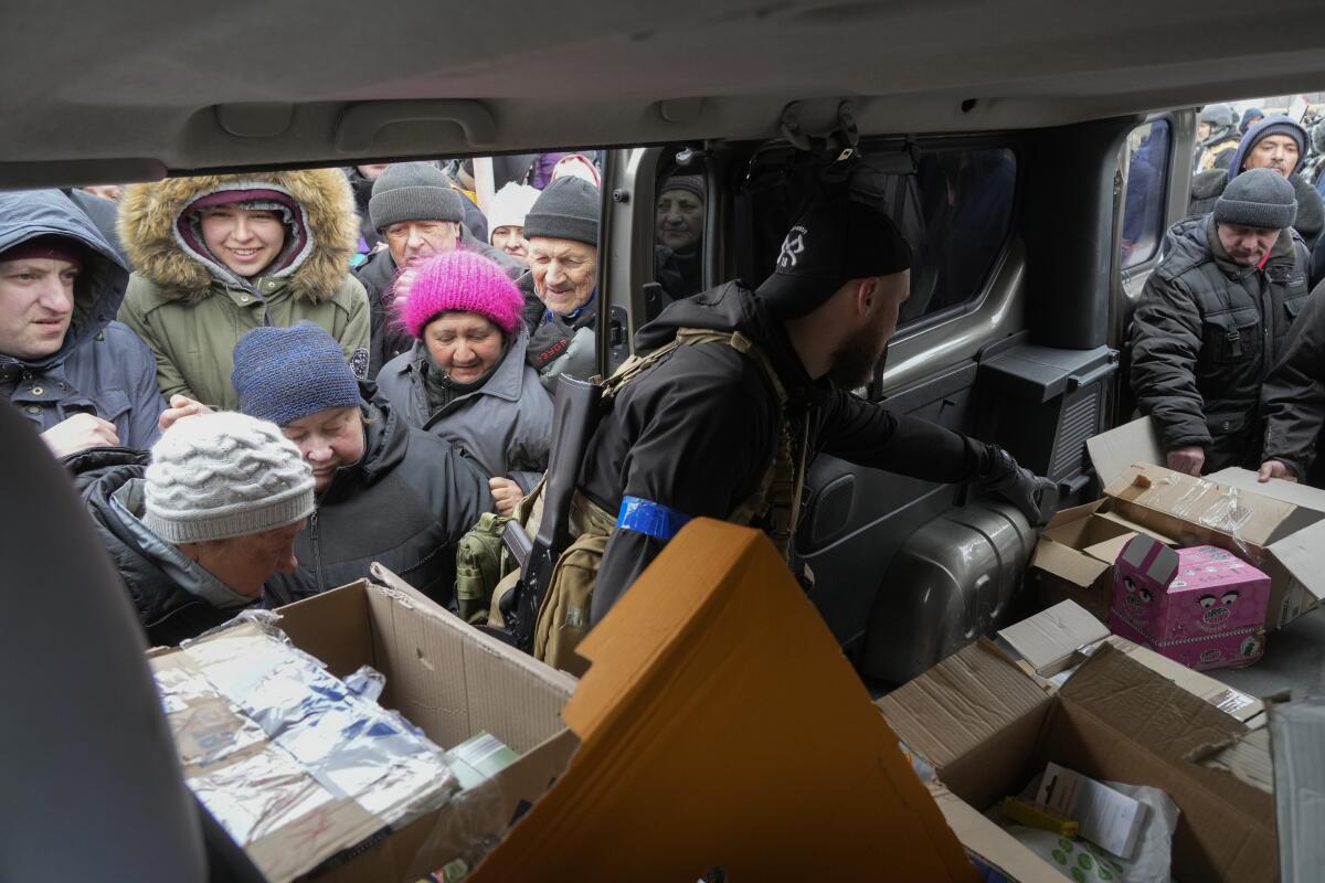 People in winter clothing and knit hats gather outside the open door of a vehicle with open boxes inside 