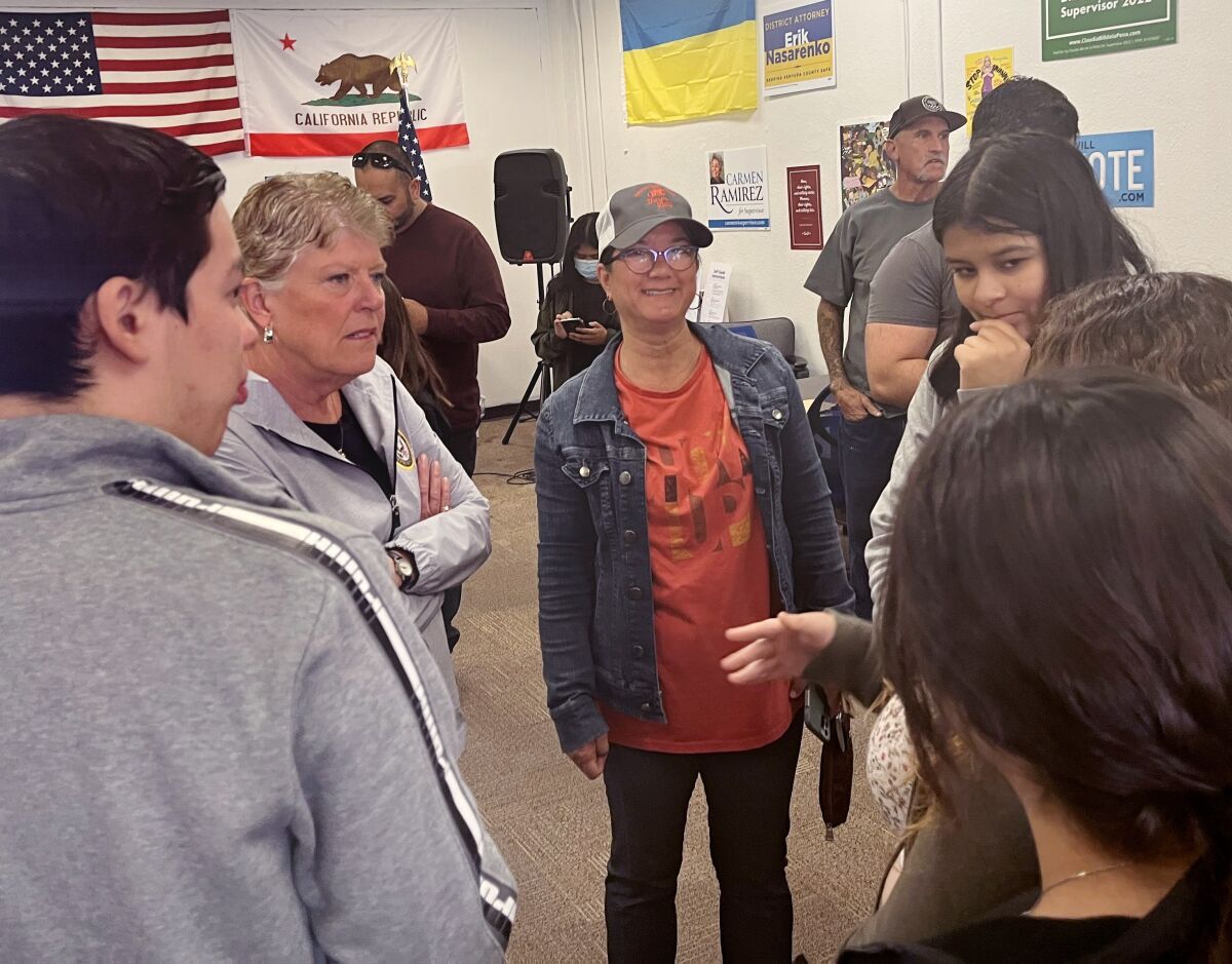 A group of people talk with U.S., California and Ukraine flags in the background