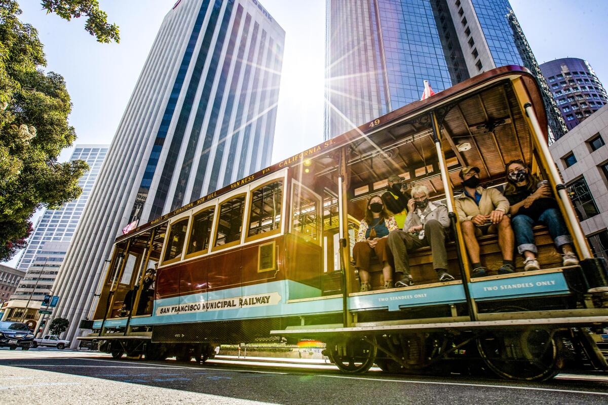 A San Francisco trolley passes tall buildings, the sun glinting between them.