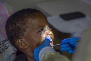 Long Beach, CA - October 12: Dental Hygienist Elizabeth Valdivia, right, cleans the teeth of Armani Allen, 2, as his mom, Nicole Nelson, of Long Beach, holds him at the Oral Health Education Center, an early intervention program that takes care of low-income children at Children's Dental Health Clinic at Children's Dental Health Clinic in Long Beach Thursday, Oct. 12, 2023. (Allen J. Schaben / Los Angeles Times)