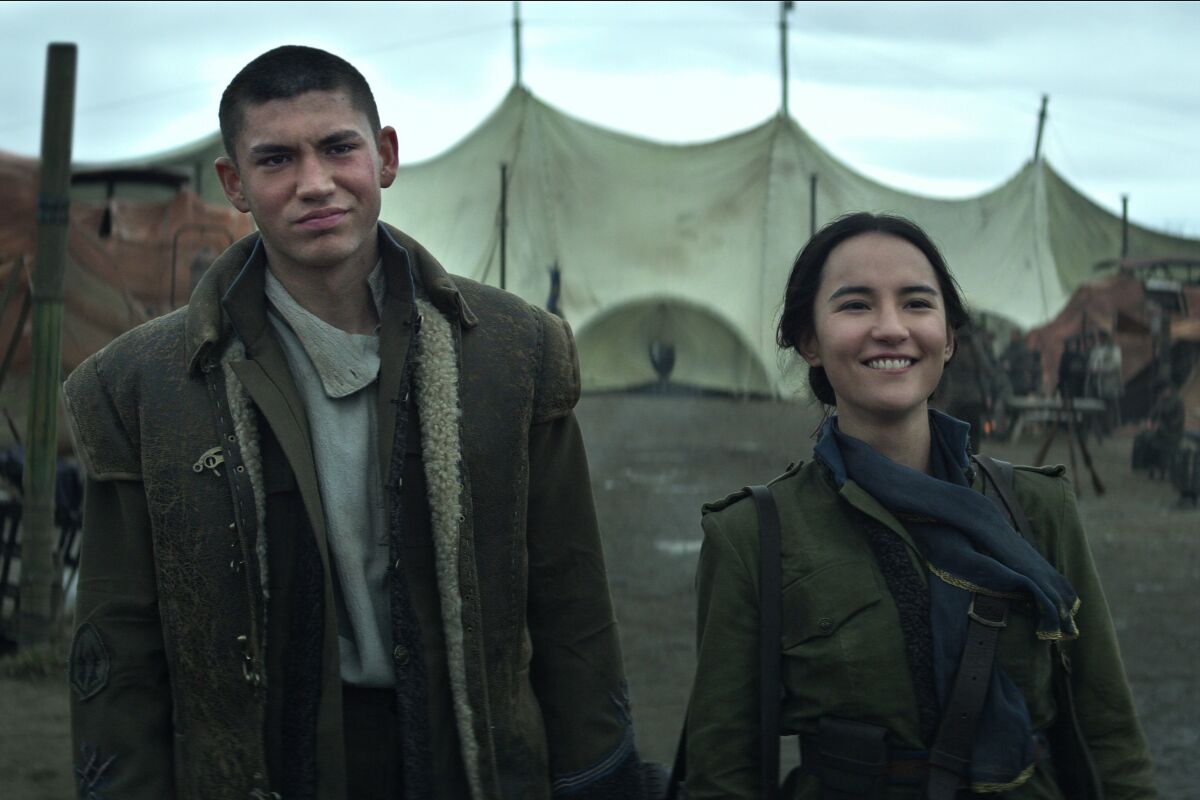 A bemused man and a smiling woman stand in a tent encampment