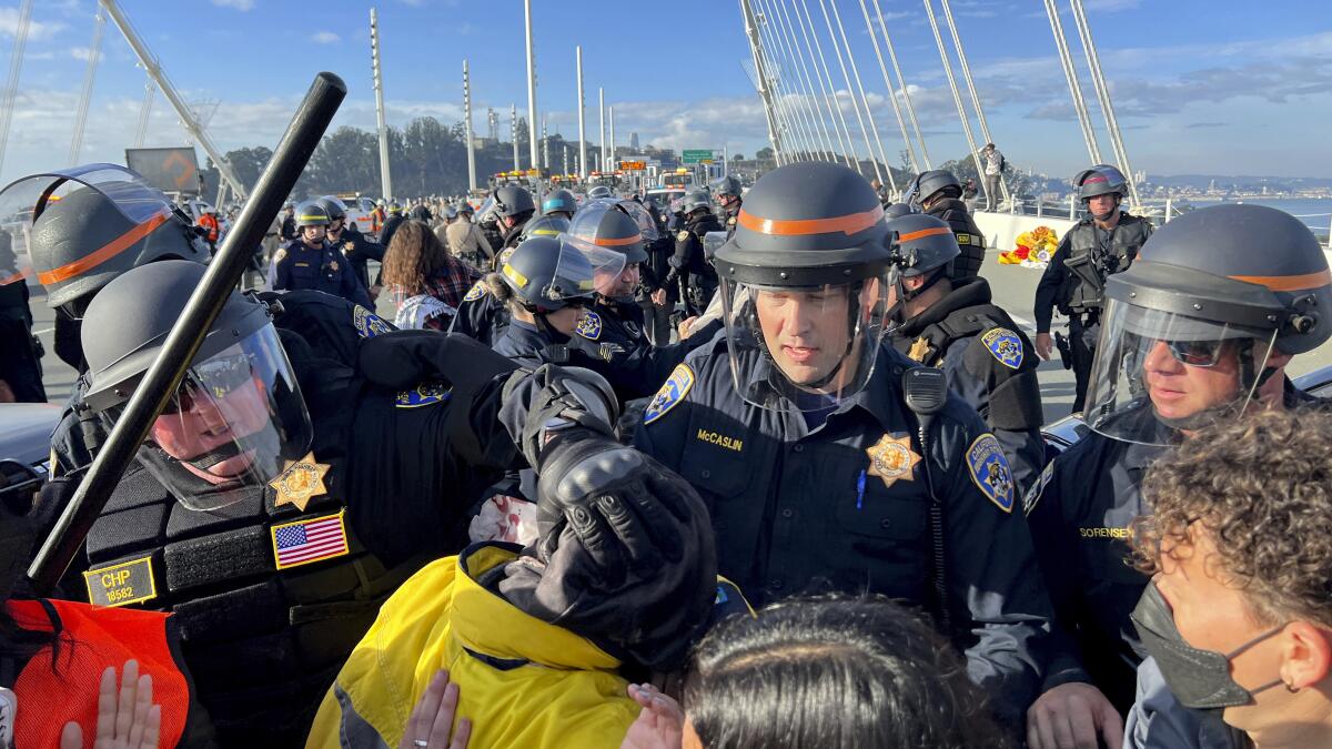 Police officers in riot gear walk through protesters on the Bay Bridge.