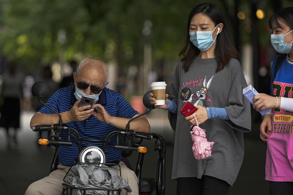 Dos mujeres con mascarillas junto a un hombre que revisa su celular, en Beijing