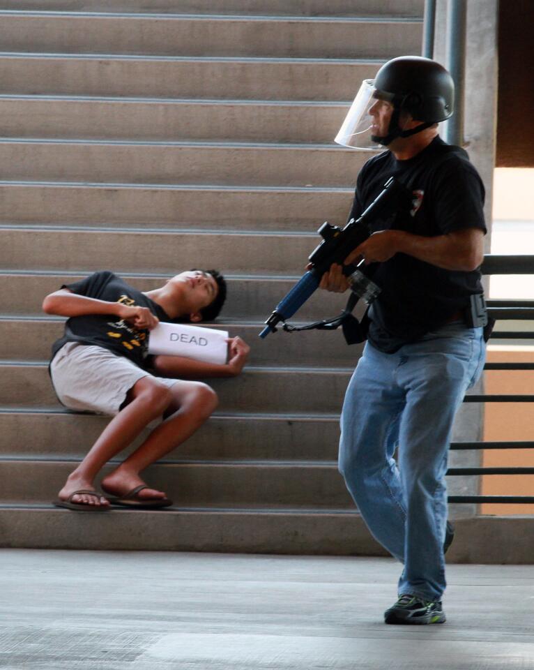 Burbank High School student Brent Min, 15, holds his dead sign as he plays the part of a victim as a Burbank police officer moves passed him in search for the shooter at Burbank High School as the Burbank Police and Fire Departments work together to run school shooter scenarios to be better prepared to work together to recover the injured for faster treatment on Thursday, August 7, 2014. (Tim Berger/Staff Photographer)