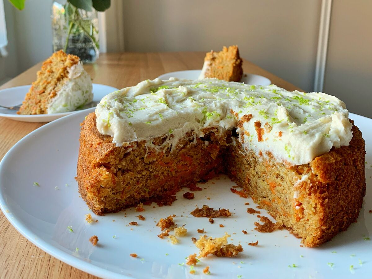A round Vegan Carrot-Banana Cake with a wedge cut out of it and a slice sitting on a plate nearby.