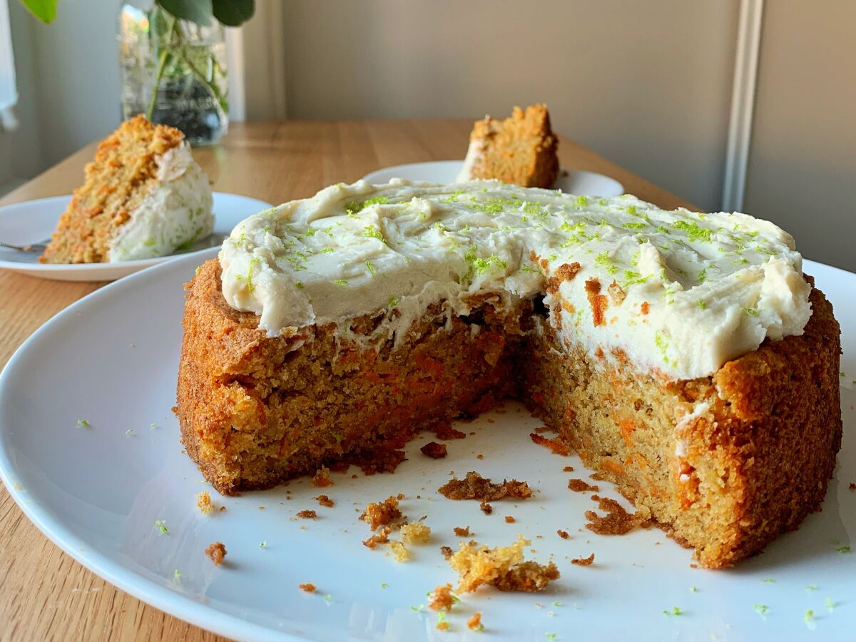 Round vegan carrot banana cake cut into wedges and a slice on a nearby plate.