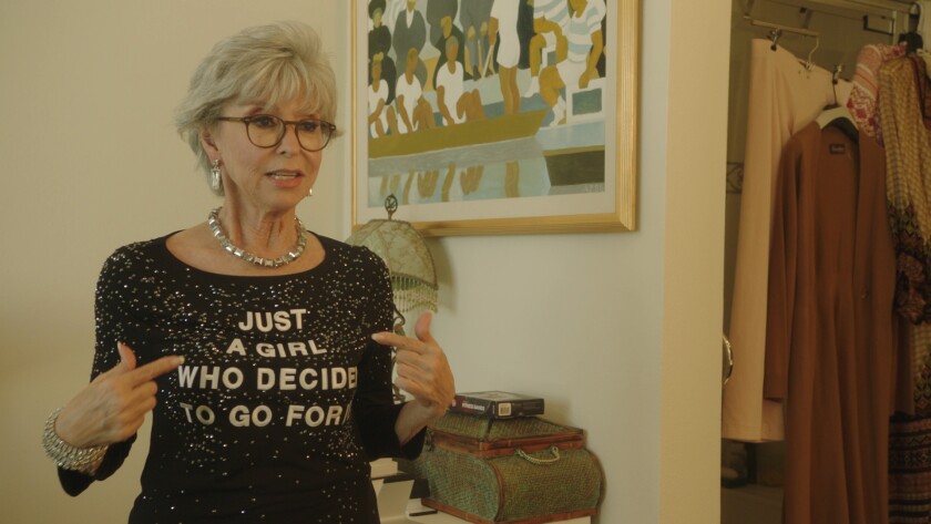 Rita Moreno points at her T-shirt, which says "Just a Girl Who Decided to Go for It."