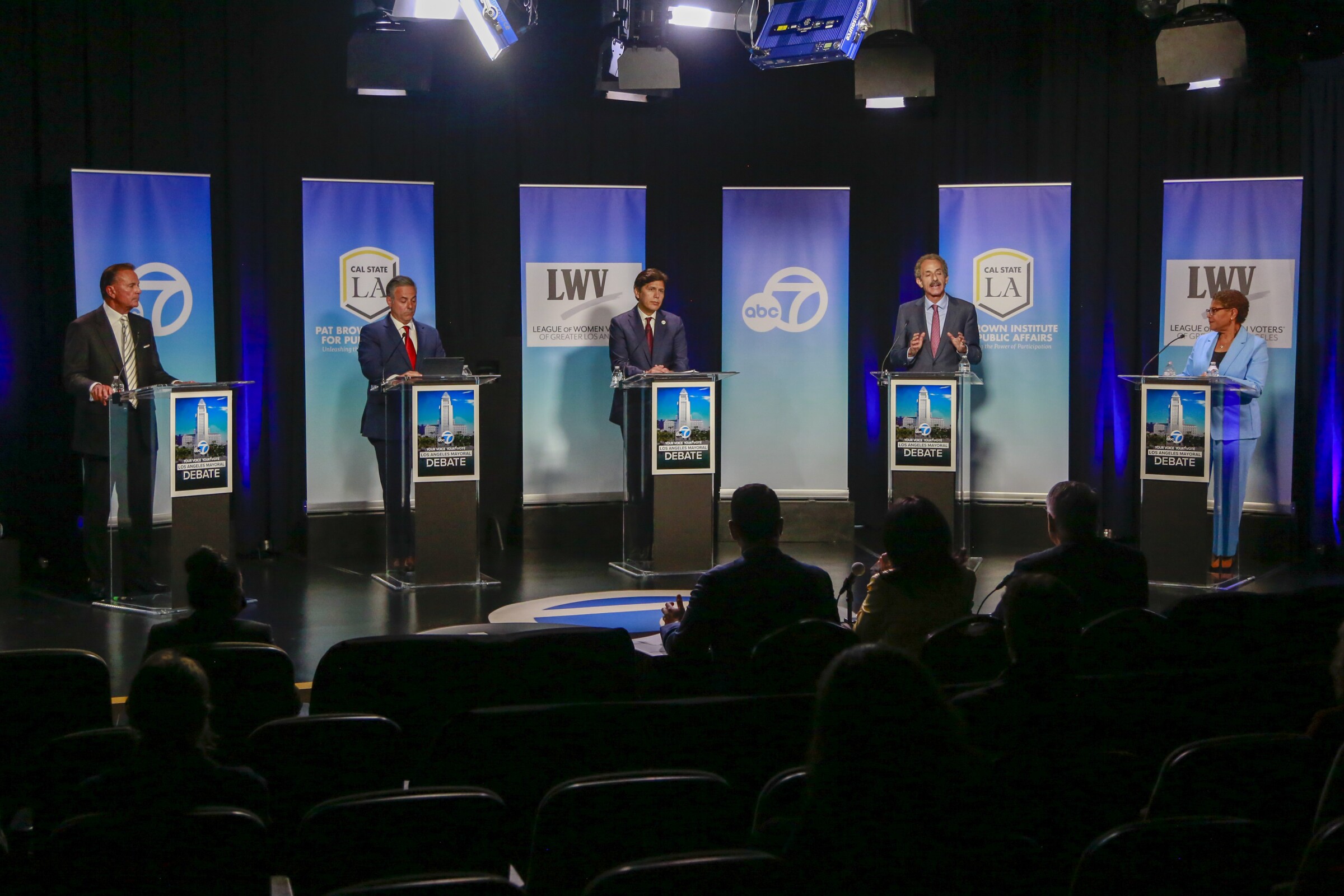 Six mayoral candidates, each standing behind a lectern, participate in a debate at Cal State L.A. 
