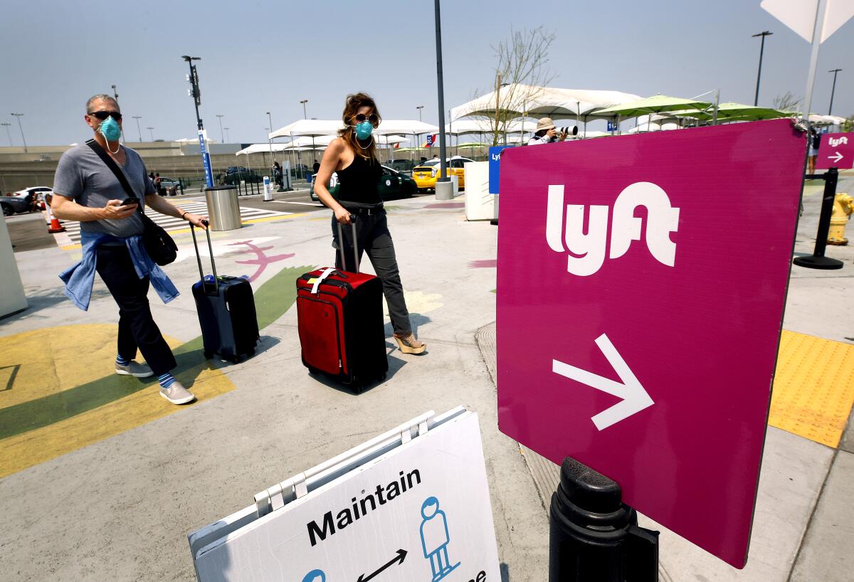Two people with luggage walk near a Lyft sign at LAX 