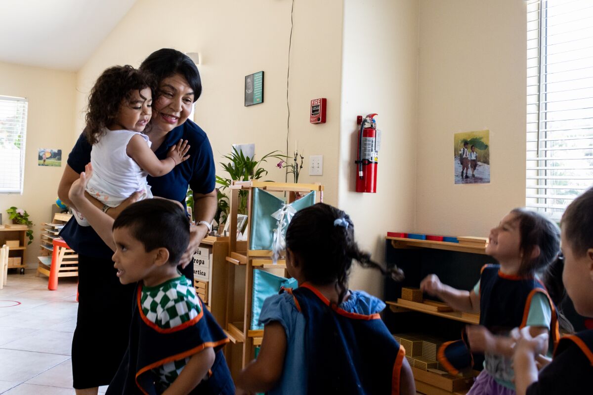 Chula Vista, CA - July 20: Karla Diaz carries Claire Fisher, 2, while she and the other children dance during "Circle Time" at Diaz's home in Chula Vista on Thursday, July 20.