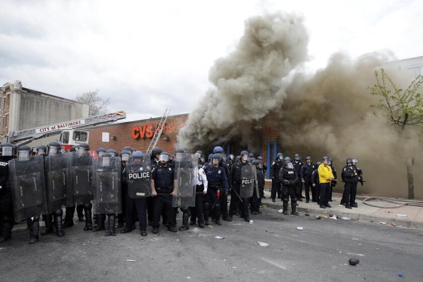Police stand in front of a burning store on April 27, 2015, during unrest following the funeral of Freddie Gray in Baltimore. Gray died from spinal injuries about a week after he was arrested and transported in a Baltimore Police Department van.