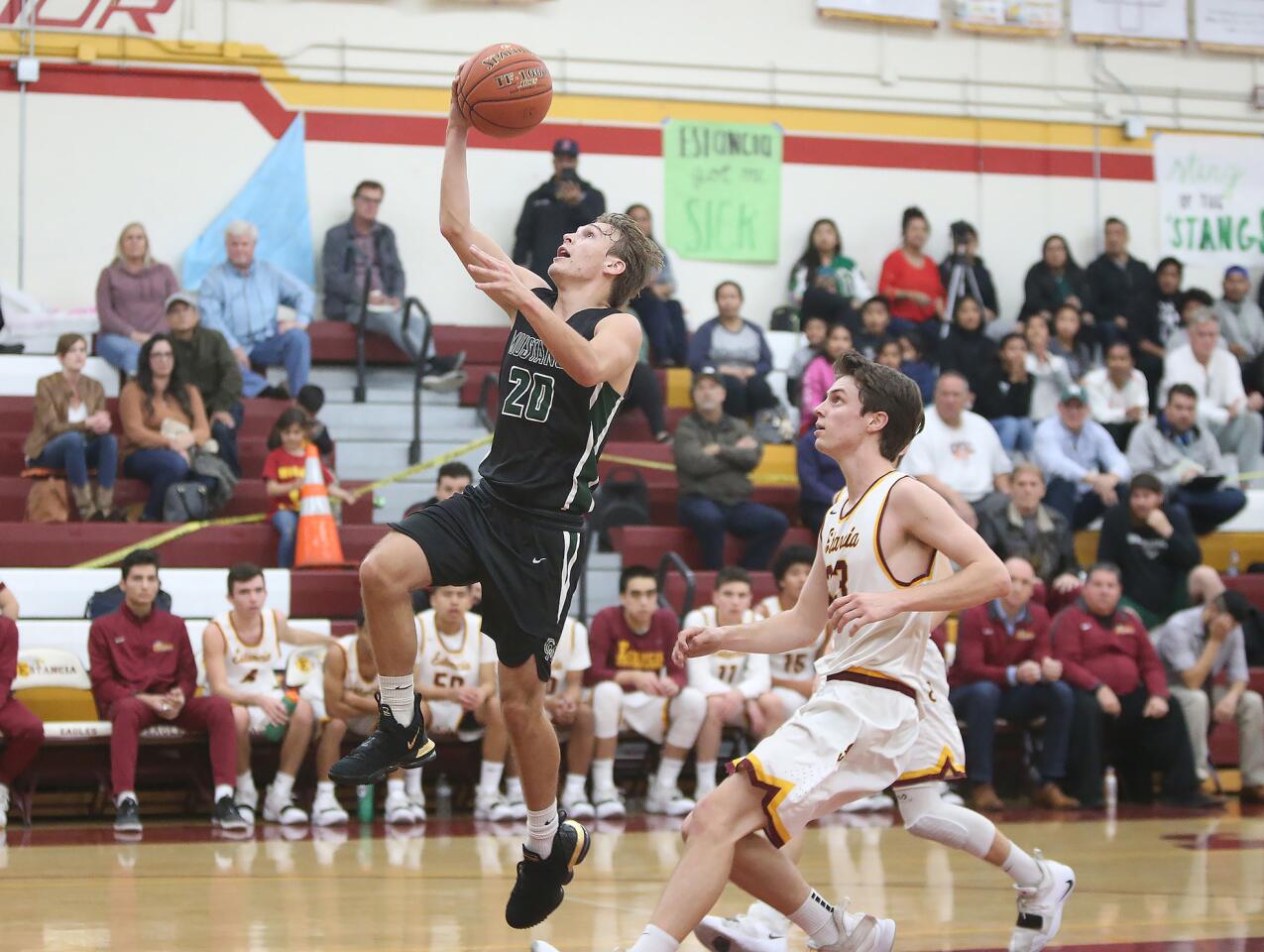 Costa Mesa High's Osman Hefner (20) drives in for a layup as Estancia's Jake Covey watches during an Orange Coast League boys' basketball game on Wednesday.
