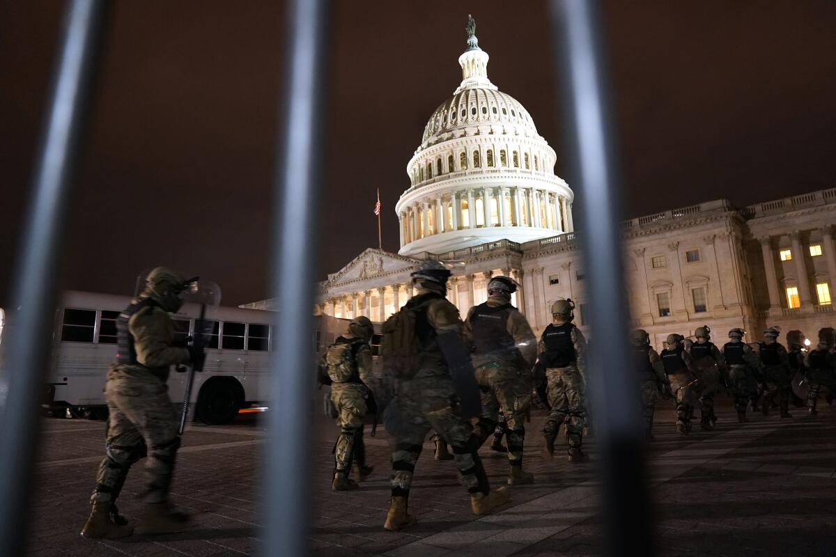 The U.S. Capitol Building is seen through a police barricade as troops march toward the building.