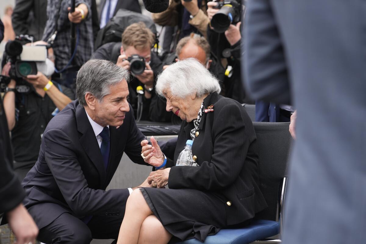 Secretary of State Antony J. Blinken, left, bends down to talk to a woman who is seated