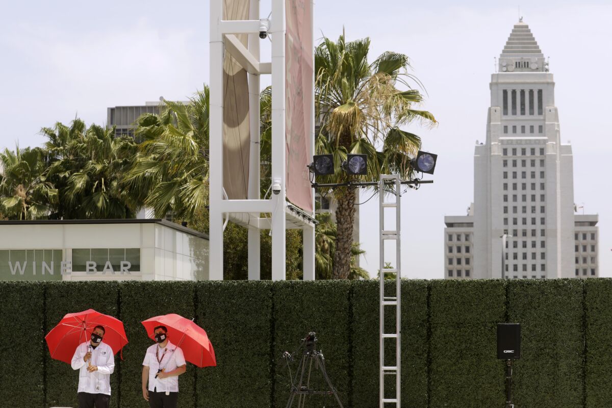 Two men stand holding umbrellas.