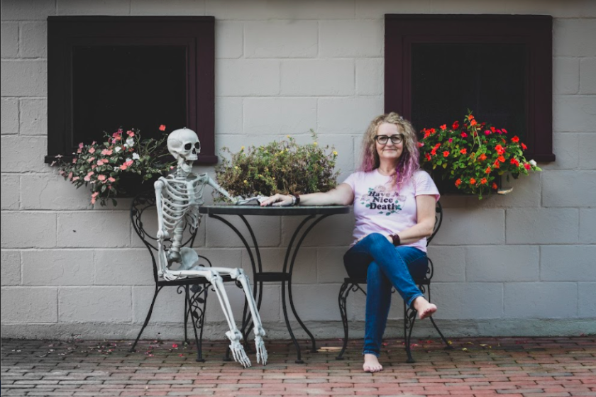 A fake skeleton and woman holding hands while sitting on patio furniture. 