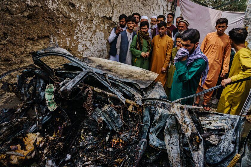 KABUL, AFGHANISTAN -- AUGUST 30, 2021: Relatives and neighbors of the Ahmadi family gathered around the incinerated husk of a vehicle targeted and hit by an U.S. drone strike that was supposed to target ISIS-K suicide bombers but instead killed 10 civilians including 7 children, in Kabul, Afghanistan, Monday, Aug. 30, 2021. (MARCUS YAM / LOS ANGELES TIMES)