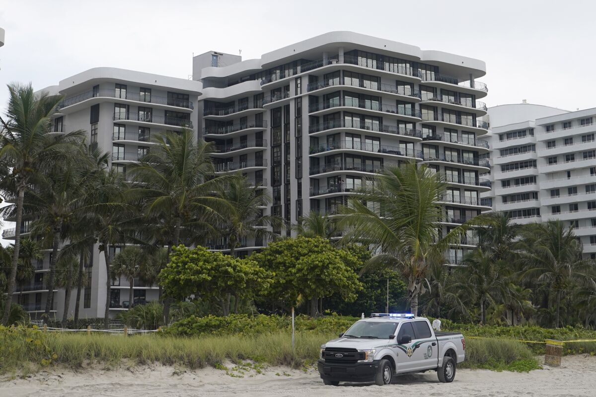 A law enforcement vehicle sits on the sand near a condo tower