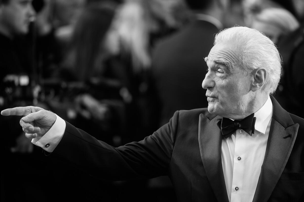 Martin Scorsese wears a tuxedo and looks to the side while pointing his finger in a black-and-white photo. 