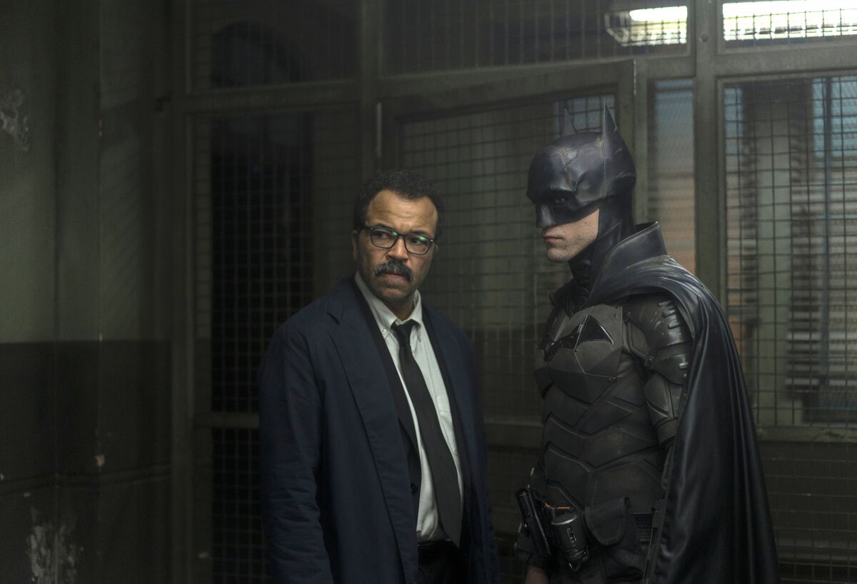 A man in a suit stands and talks with Batman.