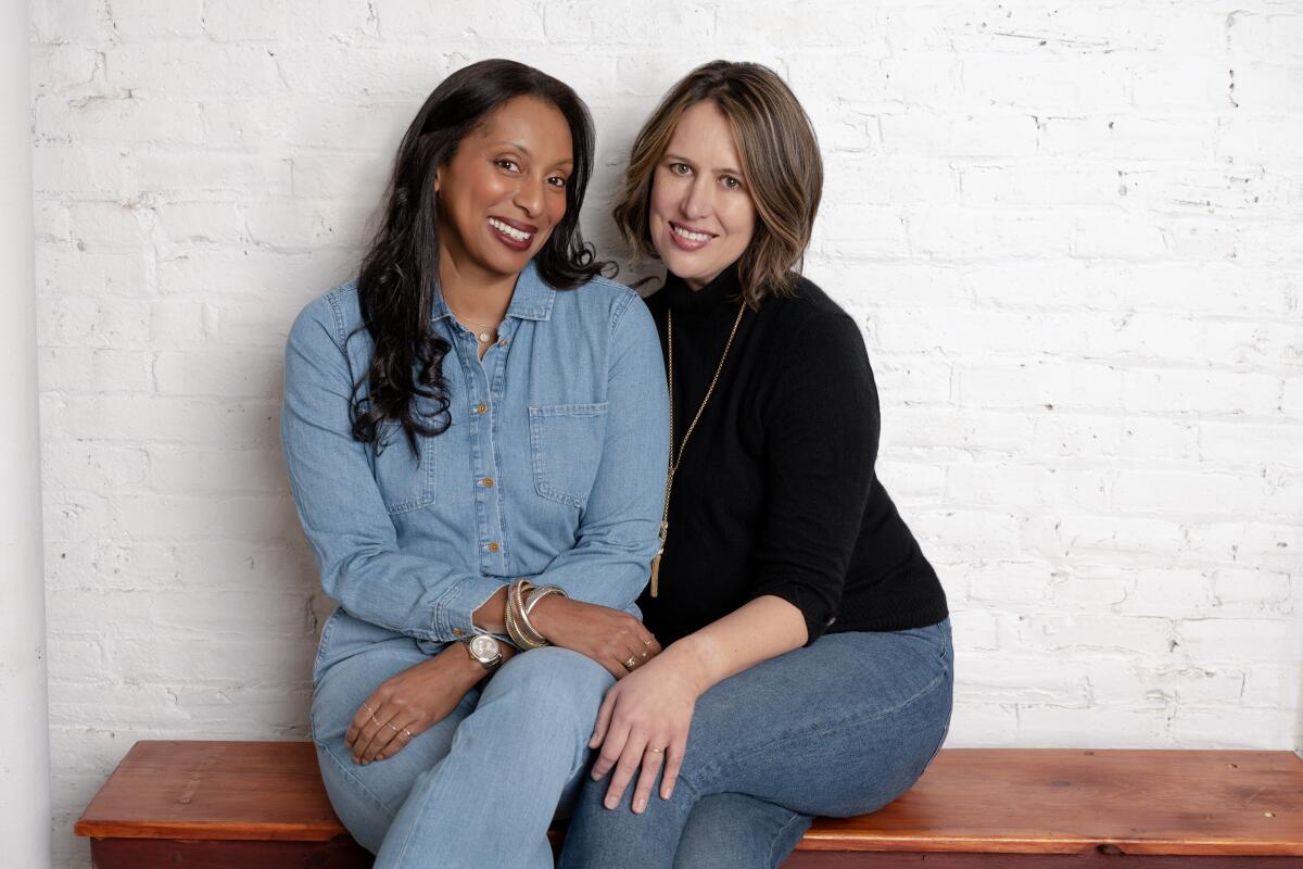 A Black woman and a white woman sit close together, smiling