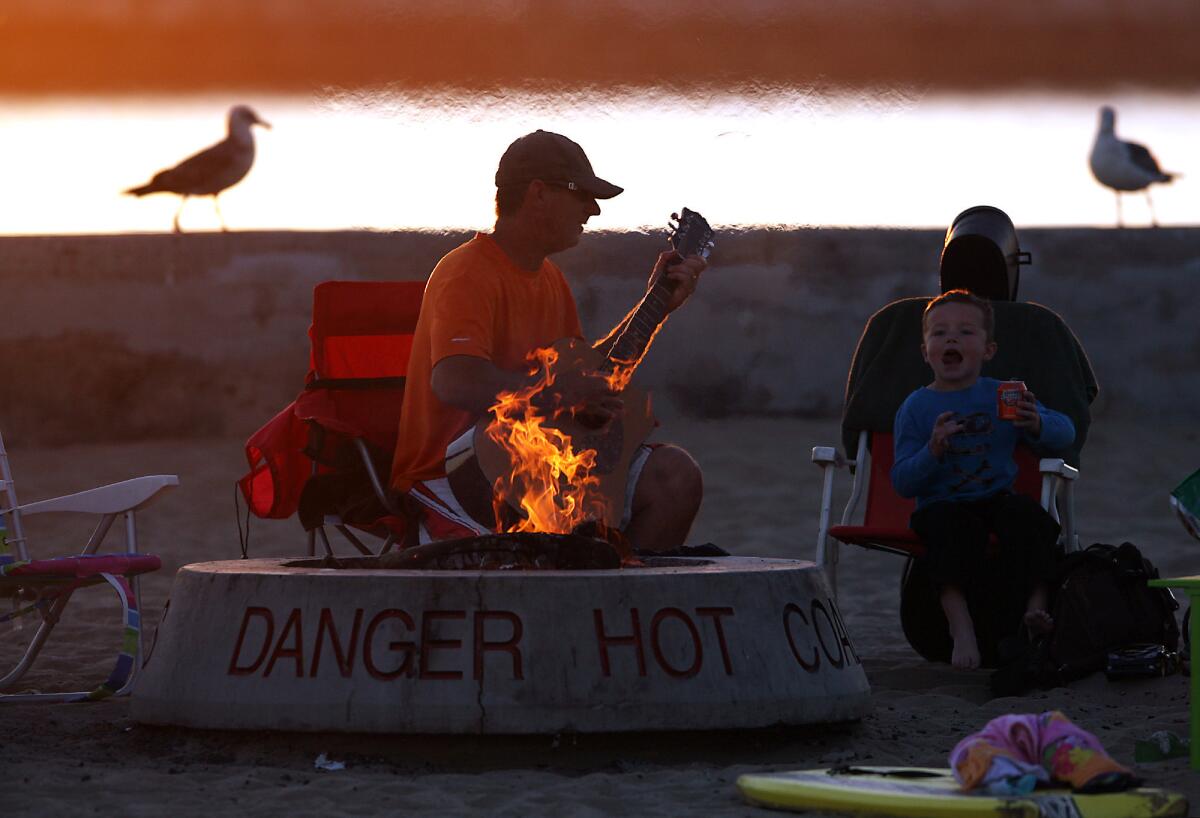 Dave Osinga and his son Zachary, 6, sit by the fire as the sun sets at Corona Del Mar State Beach.