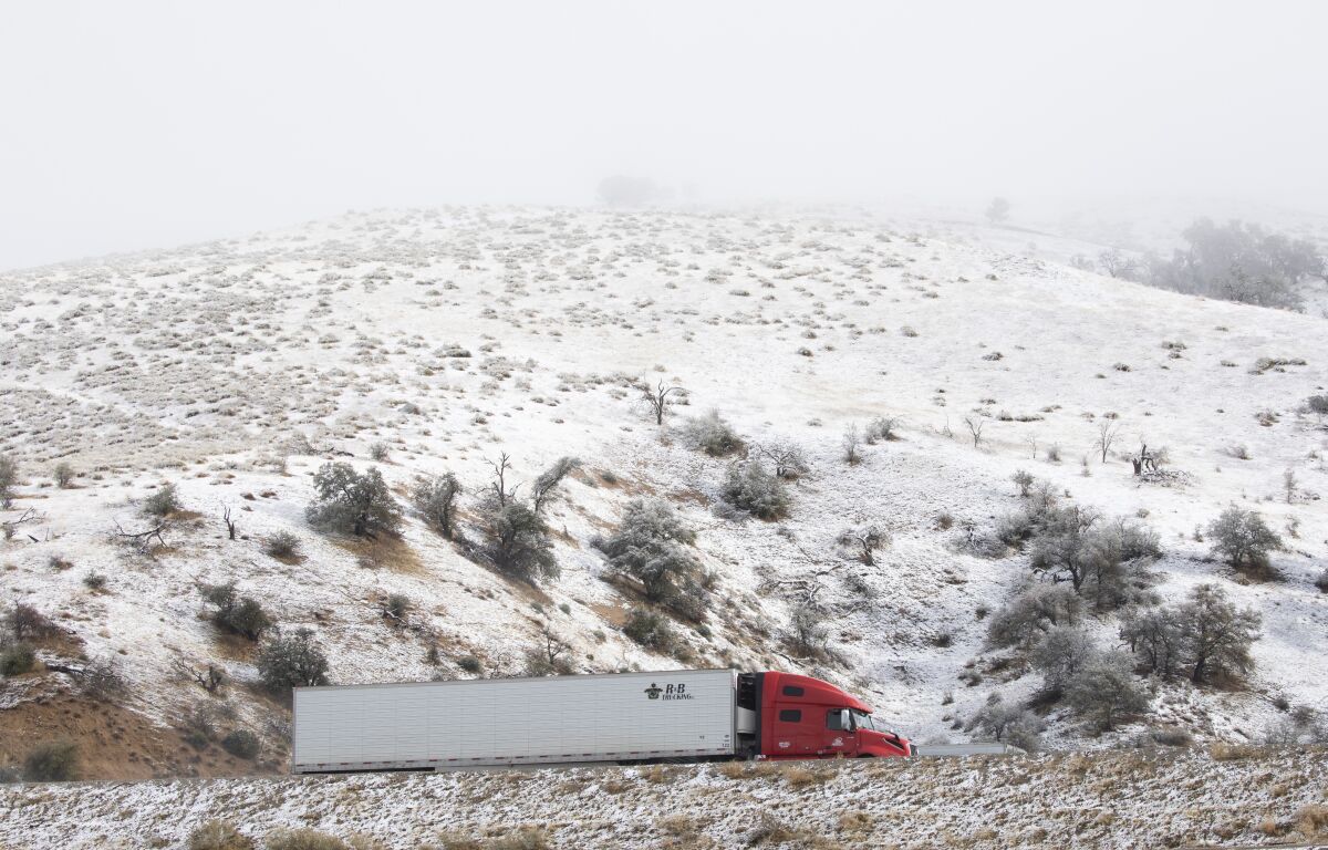 Traffic flows on Interstate 5 past snow-covered hills in Lebec, CA on Dec. 14, 2021.