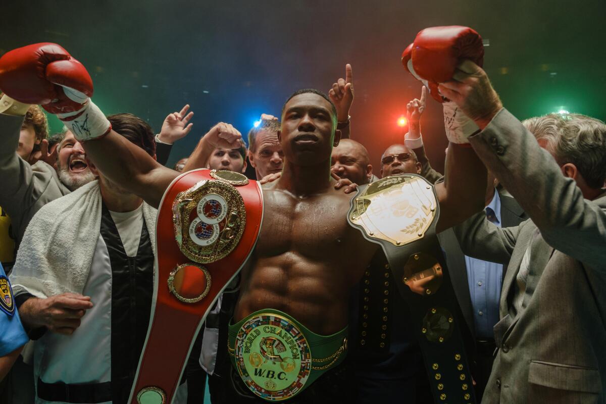 A boxer celebrating a championship victory with a crowd behind him.