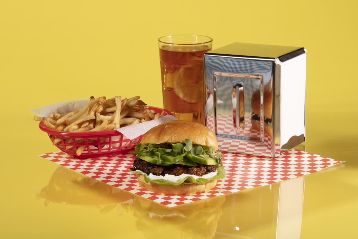 A veggie burger, basket of fries, glass of iced tea and metal napkin holder on a red-and-white checked paper placemat