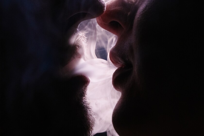 The outline of two faces very close to each other inhaling smoke
