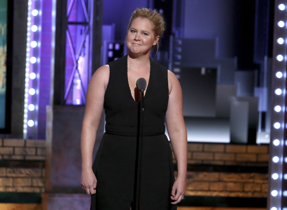 A woman in a sleeveless black dress makes a funny face onstage
