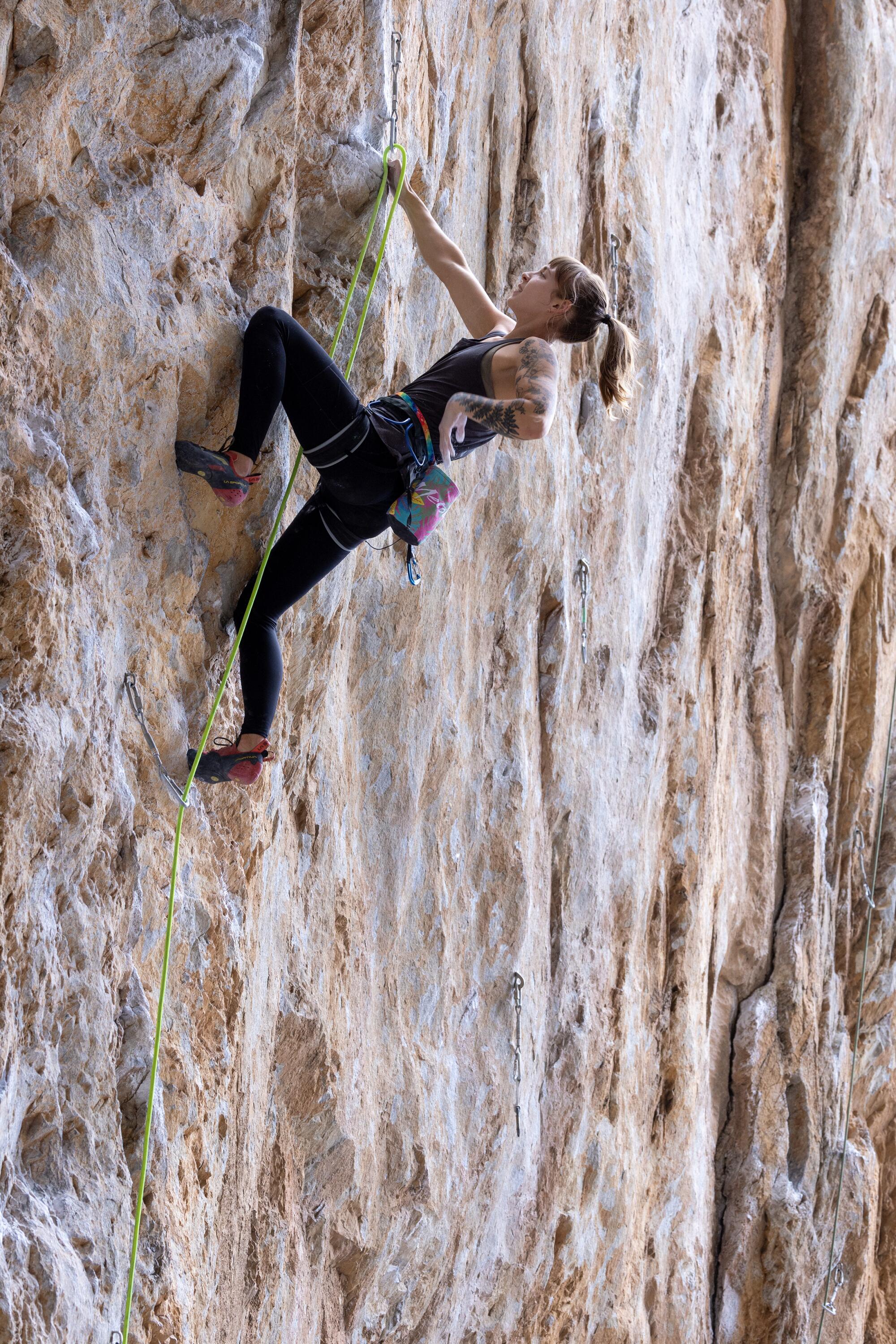 An athletic woman with blond ponytail ascends a sheer limestone wall 