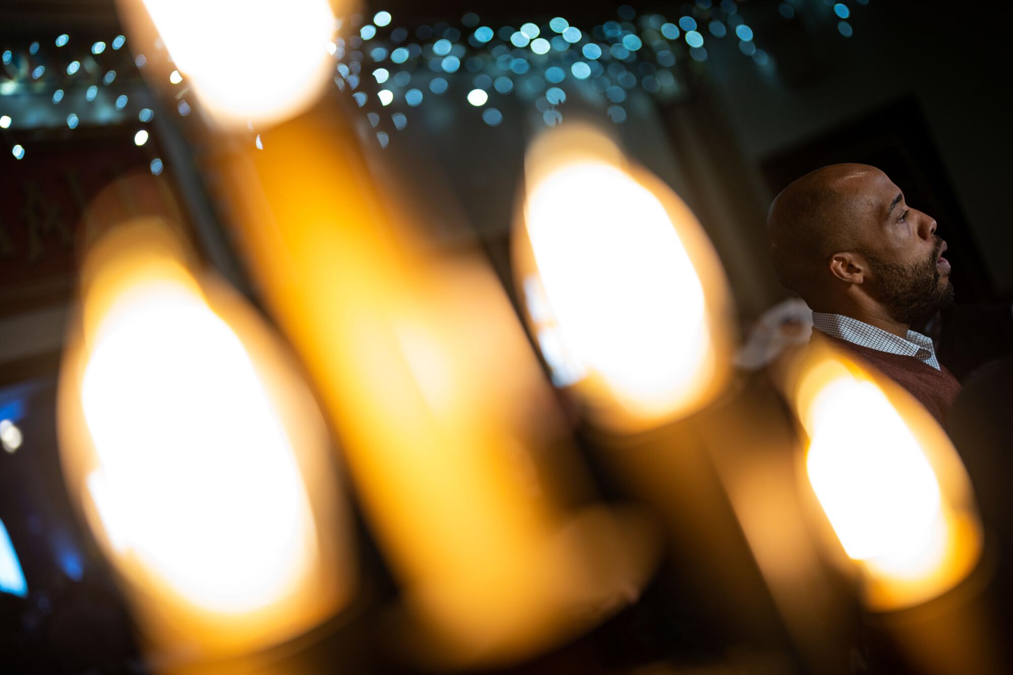 Image of an out-of-focus light fixture in the foreground and a man speaking in the background