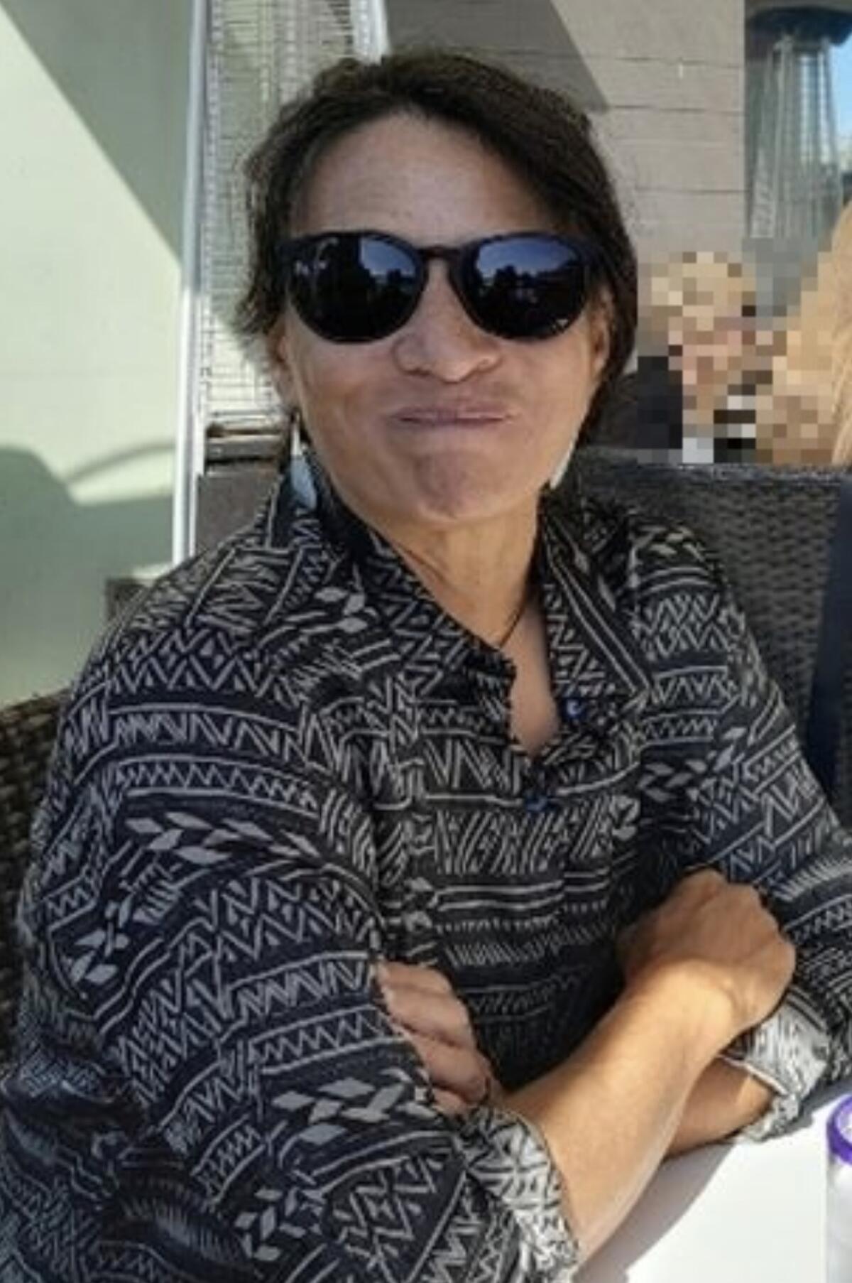 A woman wearing sunglasses smiles while folding her arms in front of her.