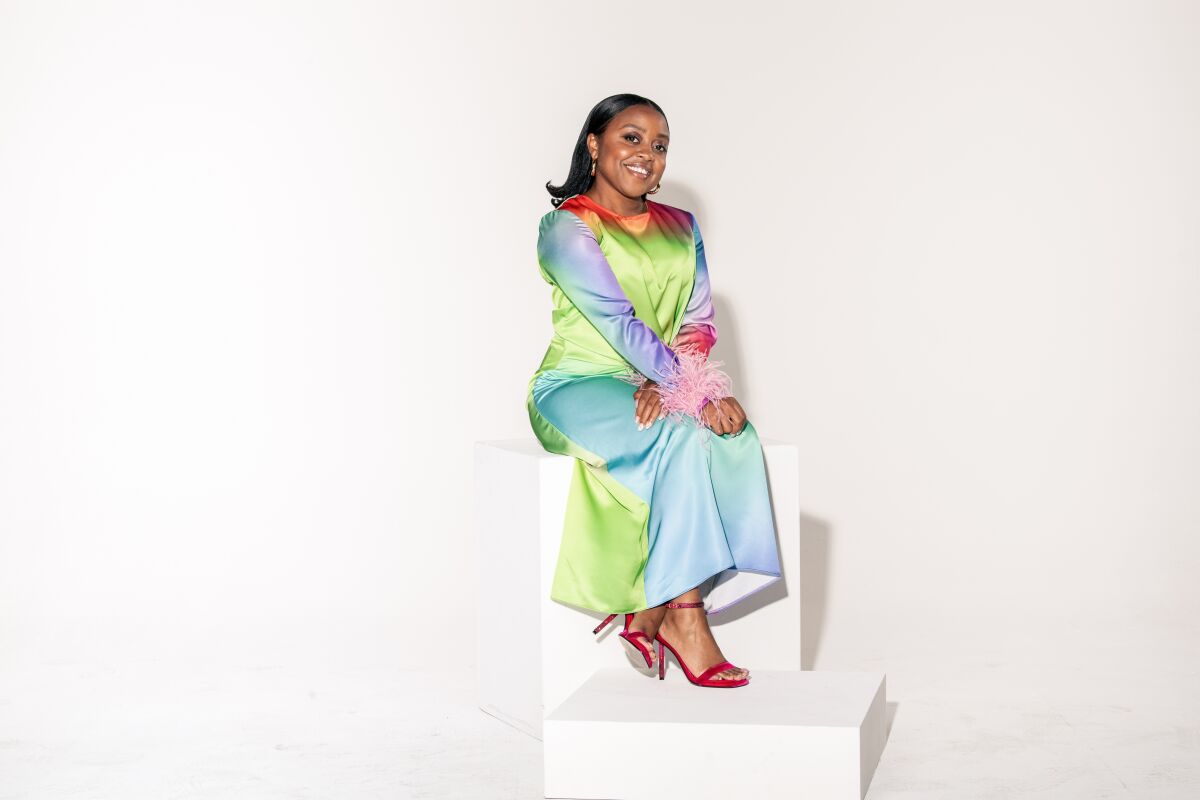 Quinta Brunson sits on giant blocks wearing a long colorful dress for a portrait.