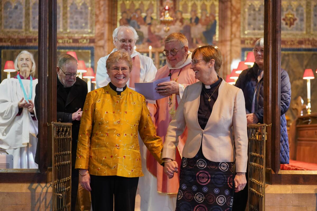 Two women hold hands standing before bishops in church