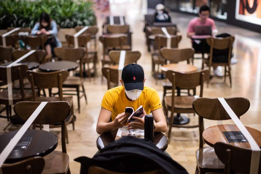 Customers sit in a cafe where social distancing between patrons has been enforced by placing white tape over unavailable tables and chairs as a precautionary measure against the COVID-19 coronavirus, in Hong Kong on March 31, 2020. (Photo by Anthony WALLACE / AFP) (Photo by ANTHONY WALLACE/AFP via Getty Images)