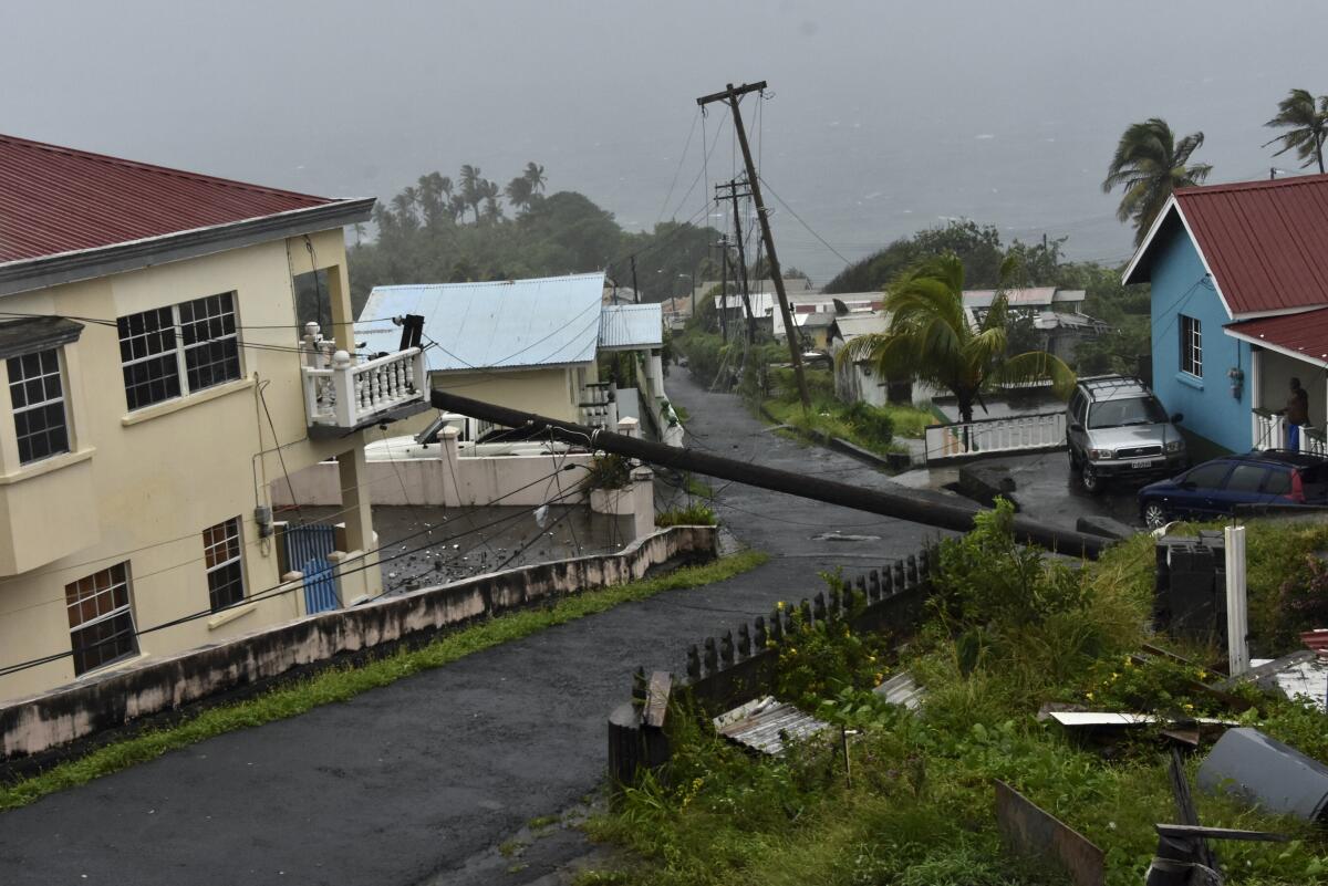 A street with a fallen electrical pole across it, its wires tangled in a balcony.