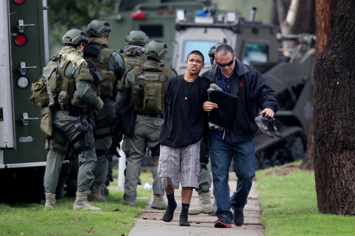 A suspect in the armed robbery of an Upland marijuana dispensary is escorted to a police vehicle after barricading himself in an apartment with two other suspects.